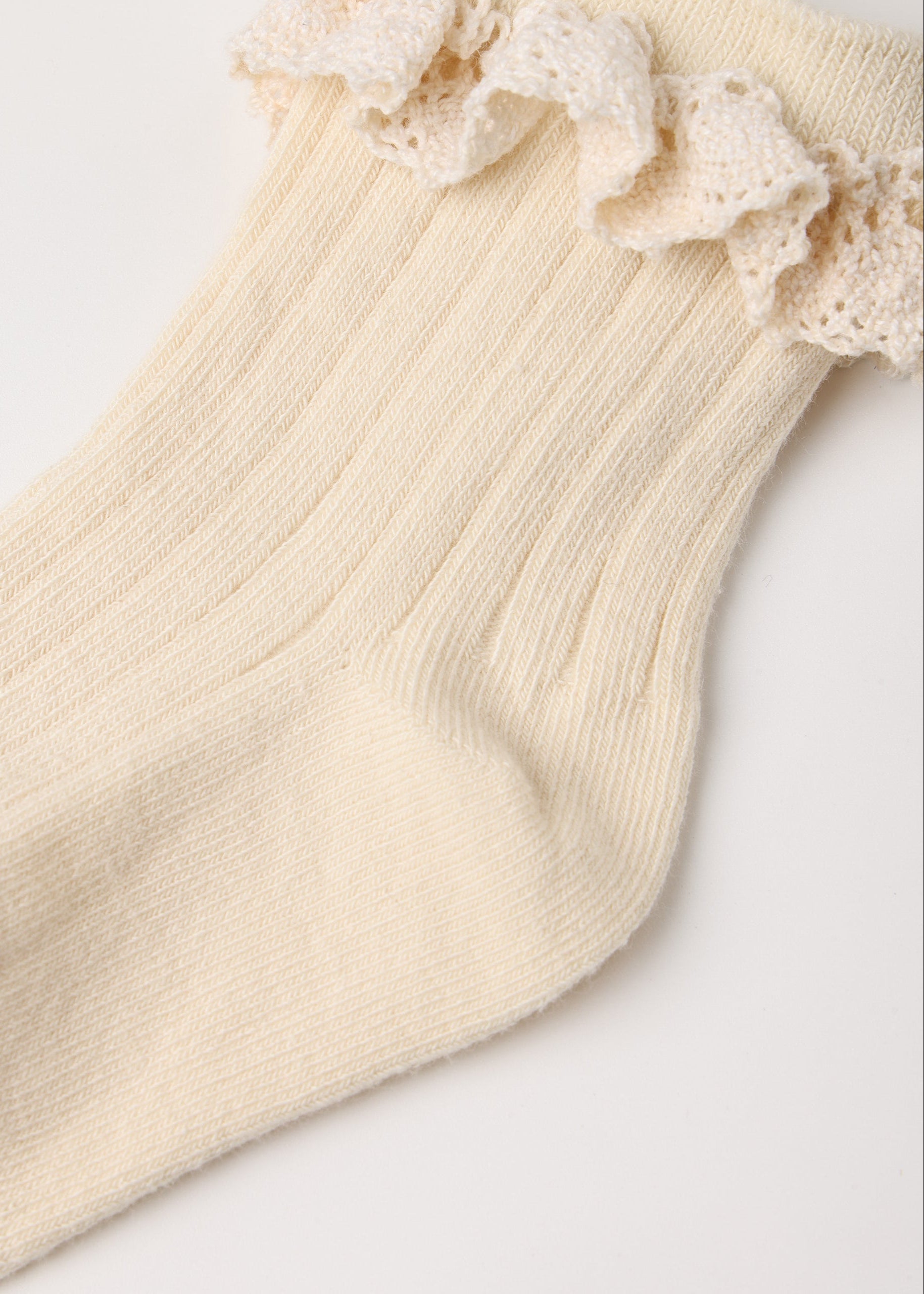 A close-up of a cream-colored ribbed knit sock with a matching lace ruffle trim at the top, laid flat on a light background.