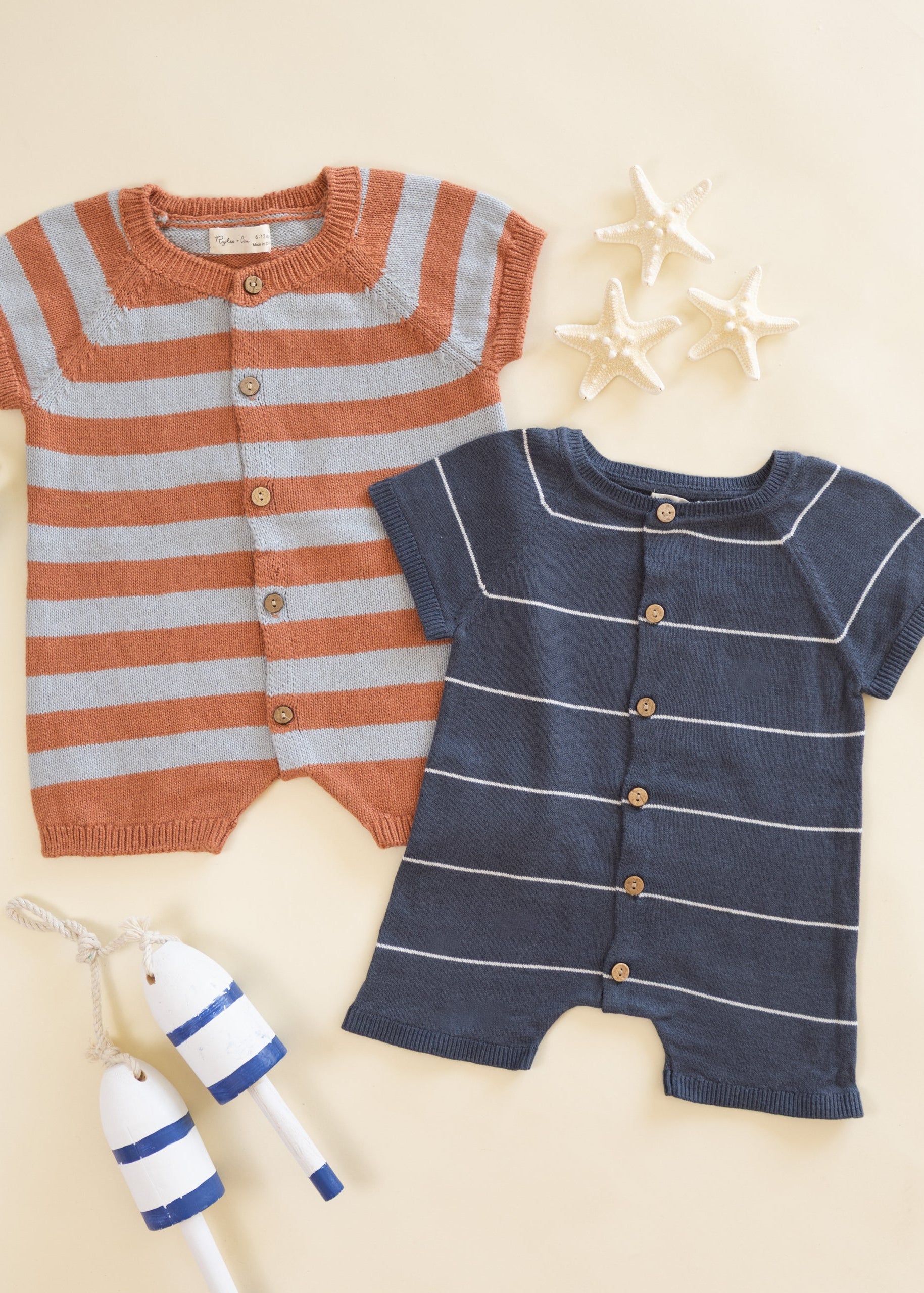 Two baby rompers, one striped orange and gray, the other navy with white stripes, on a beige background.