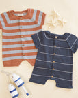 Two baby rompers, one striped orange and gray, the other navy with white stripes, on a beige background.