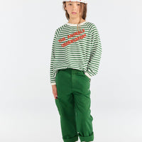 Person wearing a green and white striped shirt with red text, green pants, and blue sandals on a white background.