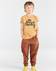 Child wearing a mustard yellow t-shirt with text and brown pants on a white background