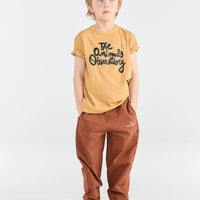 Child wearing a mustard yellow t-shirt with text and brown pants on a white background