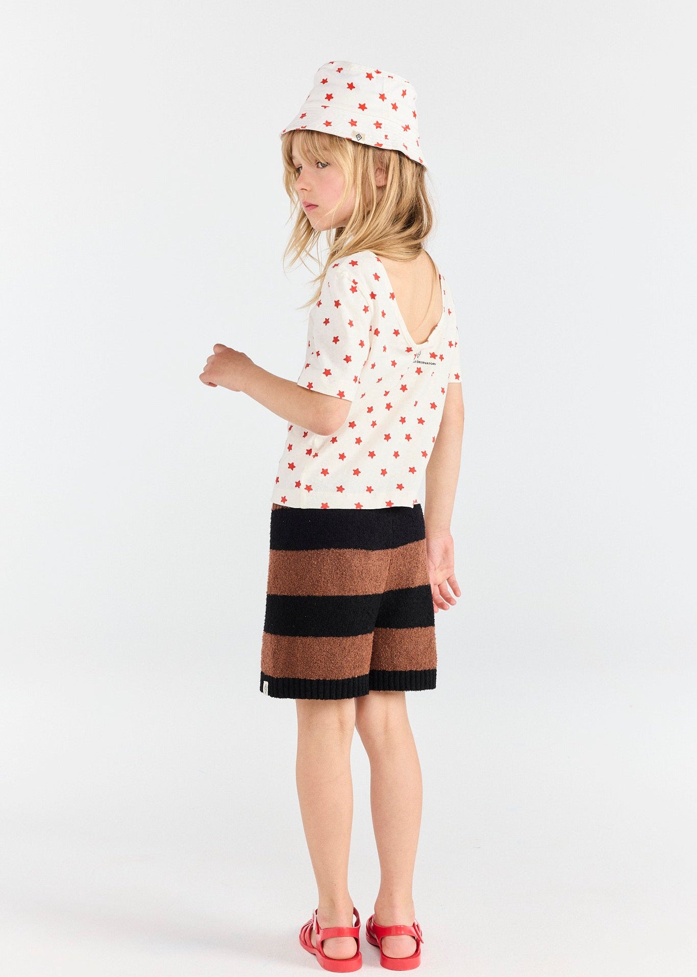 Young girl wearing a white polka dot dress with a black and brown striped skirt on a white background
