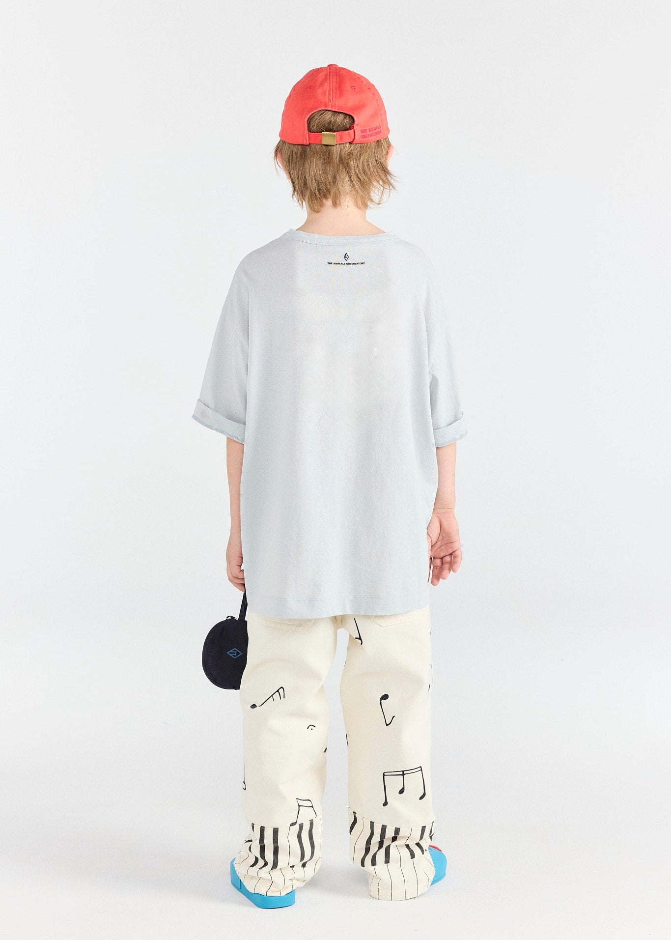 Person wearing a light blue oversized shirt, white pants with black patterns, and a red cap on a white background