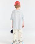 Person wearing a light blue oversized shirt, white pants with black patterns, and a red cap on a white background