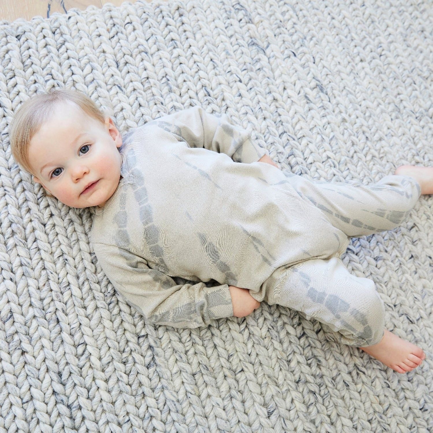 Baby lying on a textured rug wearing a patterned outfit