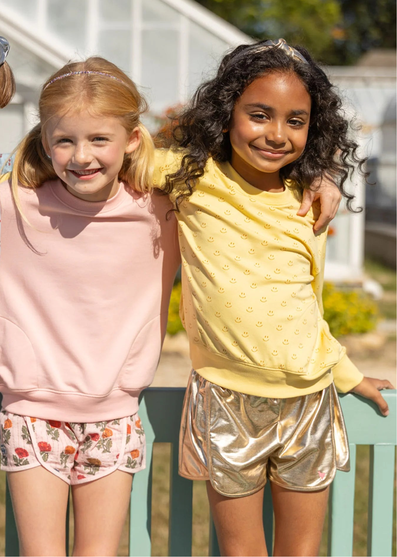 Three young girls standing together outdoors, wearing colorful outfits.