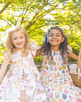 Two young girls in patterned dresses standing outdoors with a picnic basket.