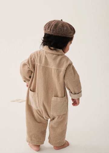 Child wearing a beige ribbed outfit and brown beret on a white background