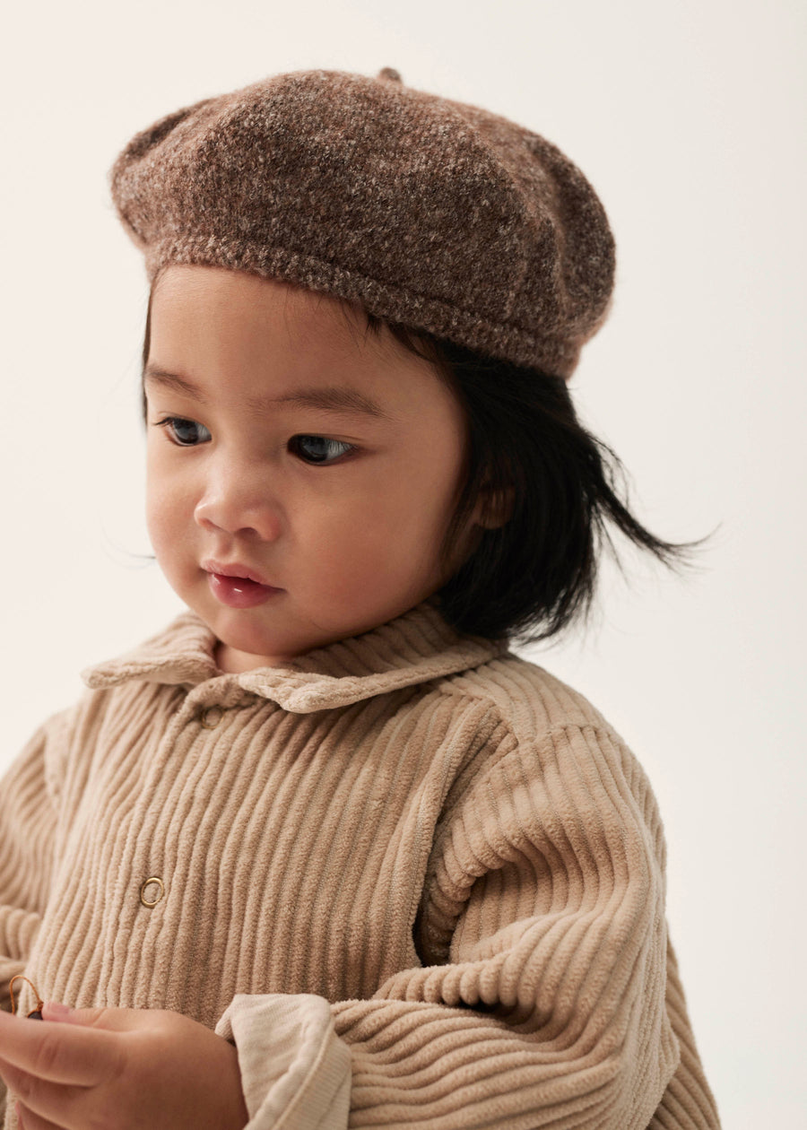 Child wearing a brown knit hat and matching outfit against a plain background