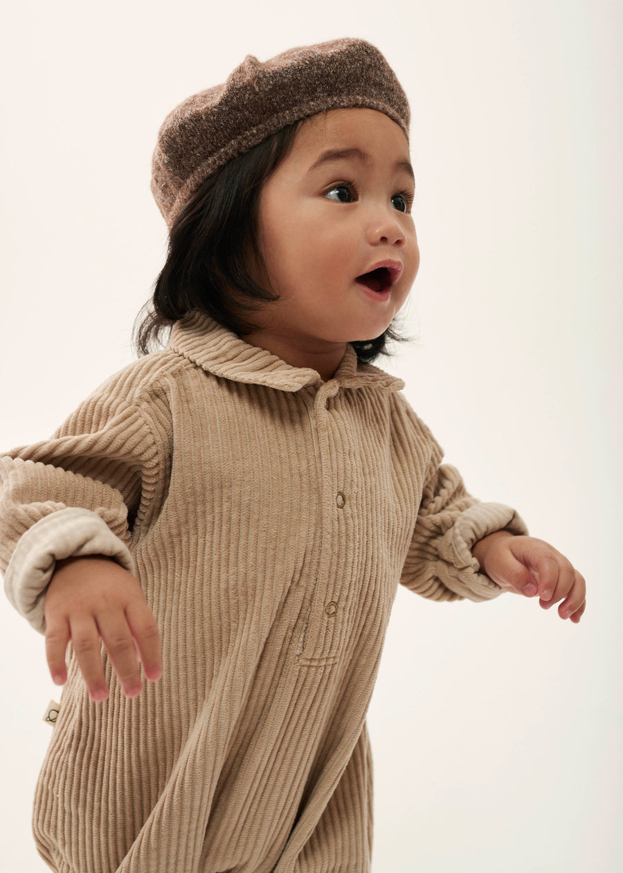 Child wearing a beige ribbed outfit and hat on a white background