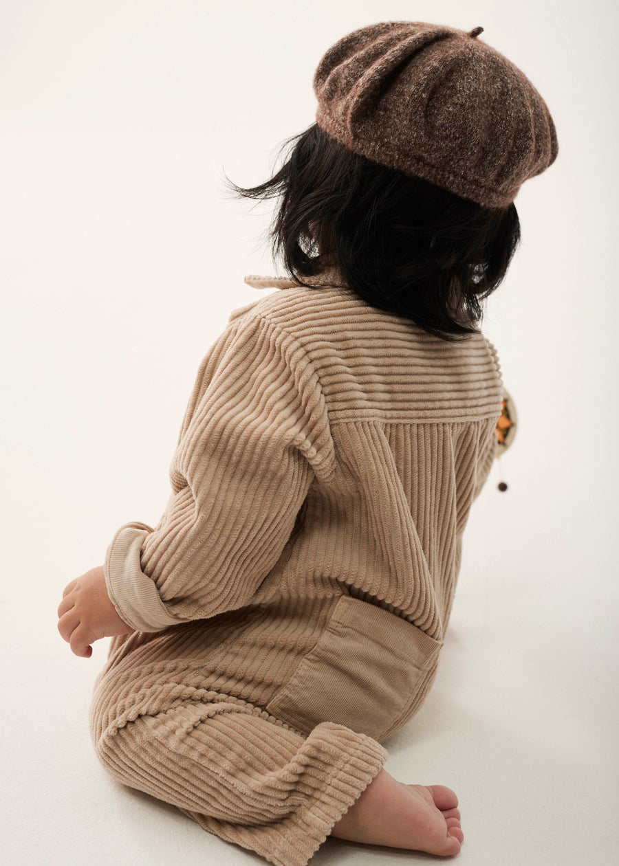 Person wearing a beige knitted outfit and brown beret on a white background