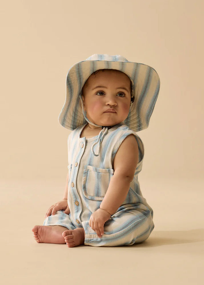 Baby wearing a striped romper and hat on a beige background