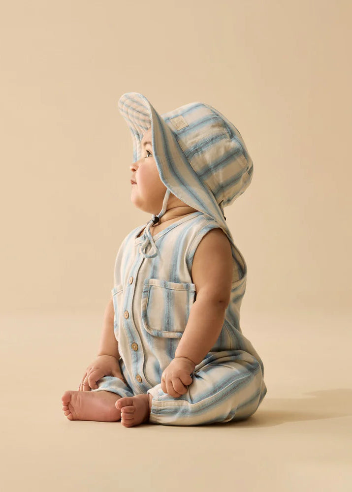 Baby wearing a striped romper and bonnet on a beige background