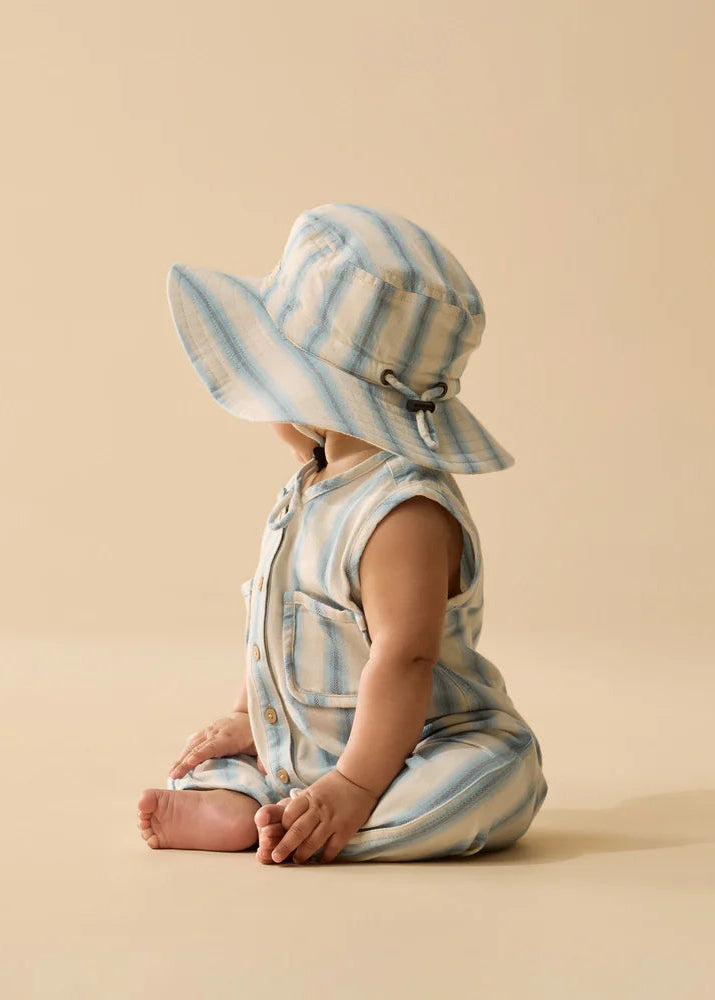 Baby in a striped romper and sun hat sitting on a beige background