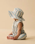 Baby in a striped romper and sun hat sitting on a beige background