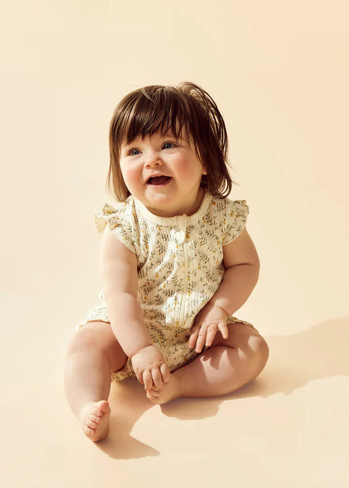 Baby sitting on a beige surface wearing a lace romper.