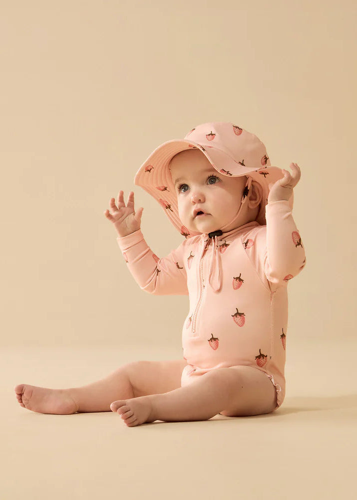 Baby in pink outfit and hat sitting on a beige background