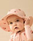 Baby wearing a pink sun hat and matching outfit with strawberry pattern on a beige background