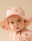 Child wearing a pink sun hat and jacket with strawberry pattern on a beige background