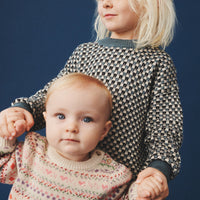 Two children wearing patterned sweaters against a dark blue background