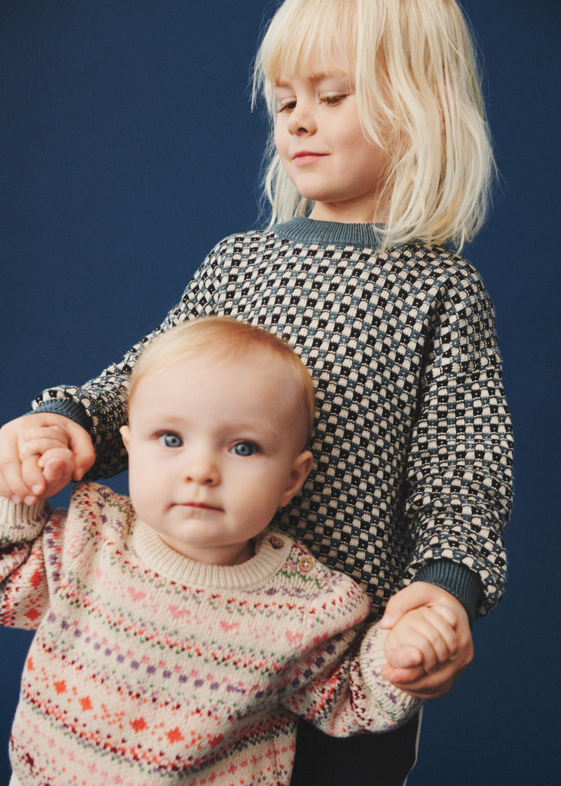 Two children wearing patterned sweaters against a dark blue background