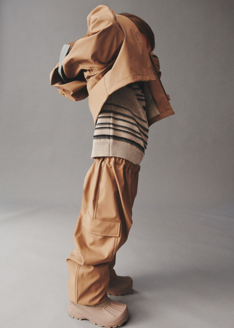 Person wearing a beige outfit with a hood and pants on a plain background