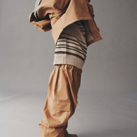Person wearing a beige outfit with a hood and pants on a plain background