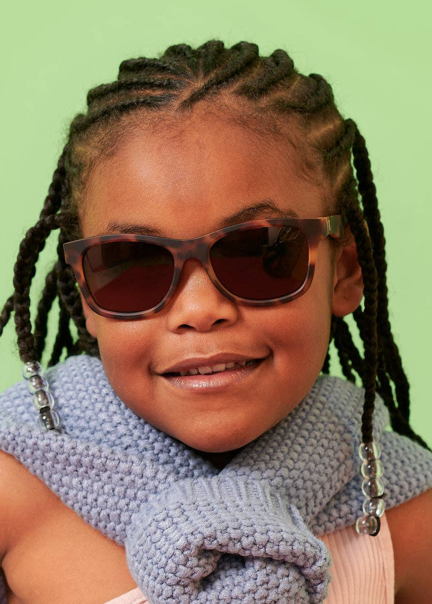 Child wearing sunglasses and a blue scarf against a green background