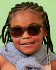 Child wearing sunglasses and a blue scarf against a green background