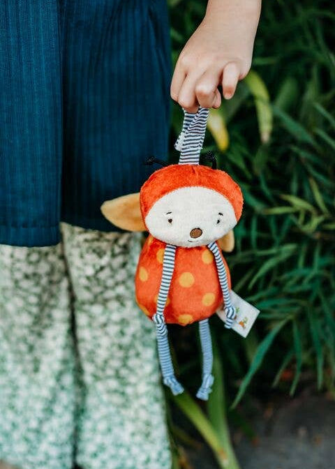 Child holding a small plush toy with an orange outfit and red hat against a natural background.