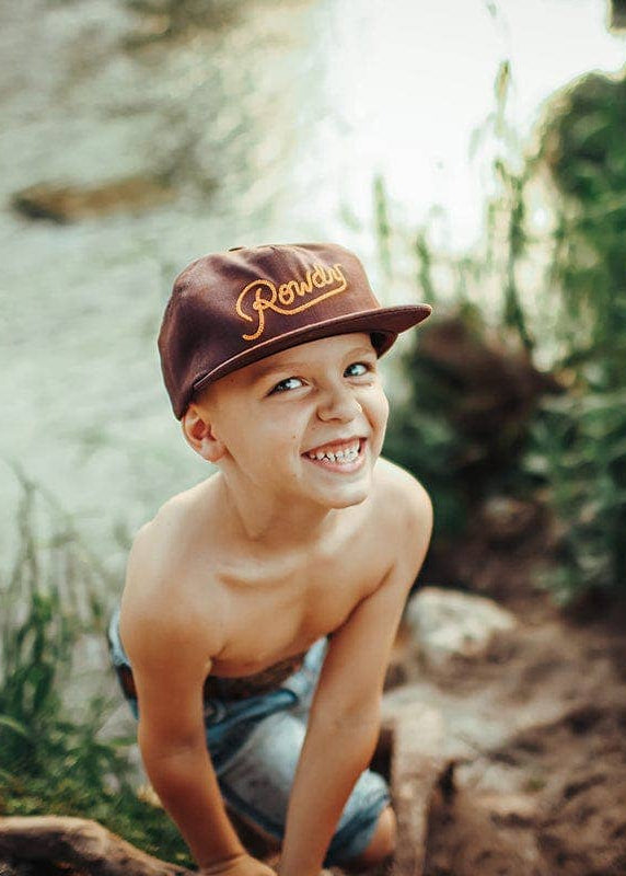 Young boy wearing a cap by a river with greenery around