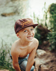Young boy wearing a cap by a river with greenery around