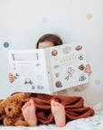 Child reading a book with a teddy bear on a bed