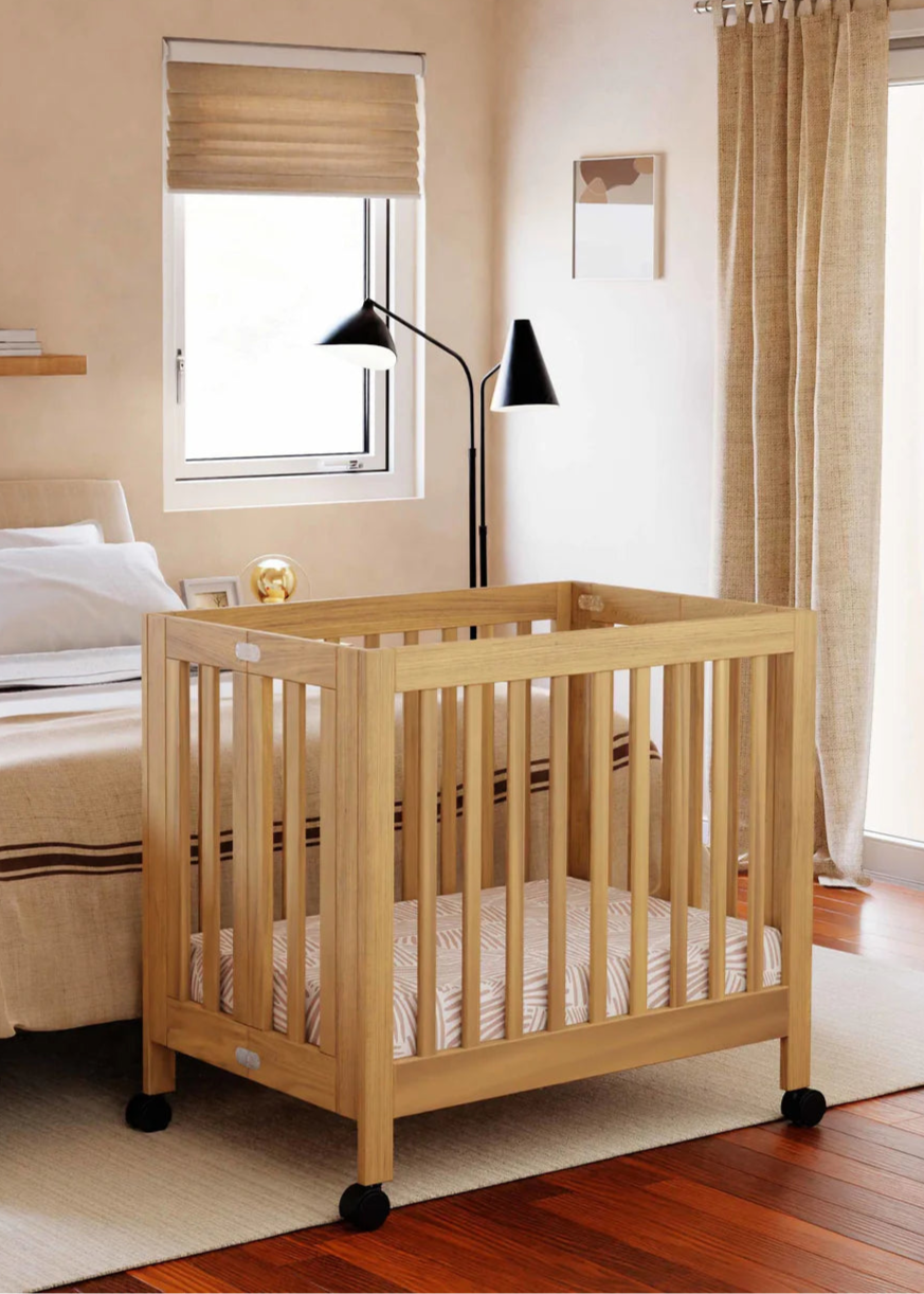 Wooden crib in a bedroom with a bed and window in the background