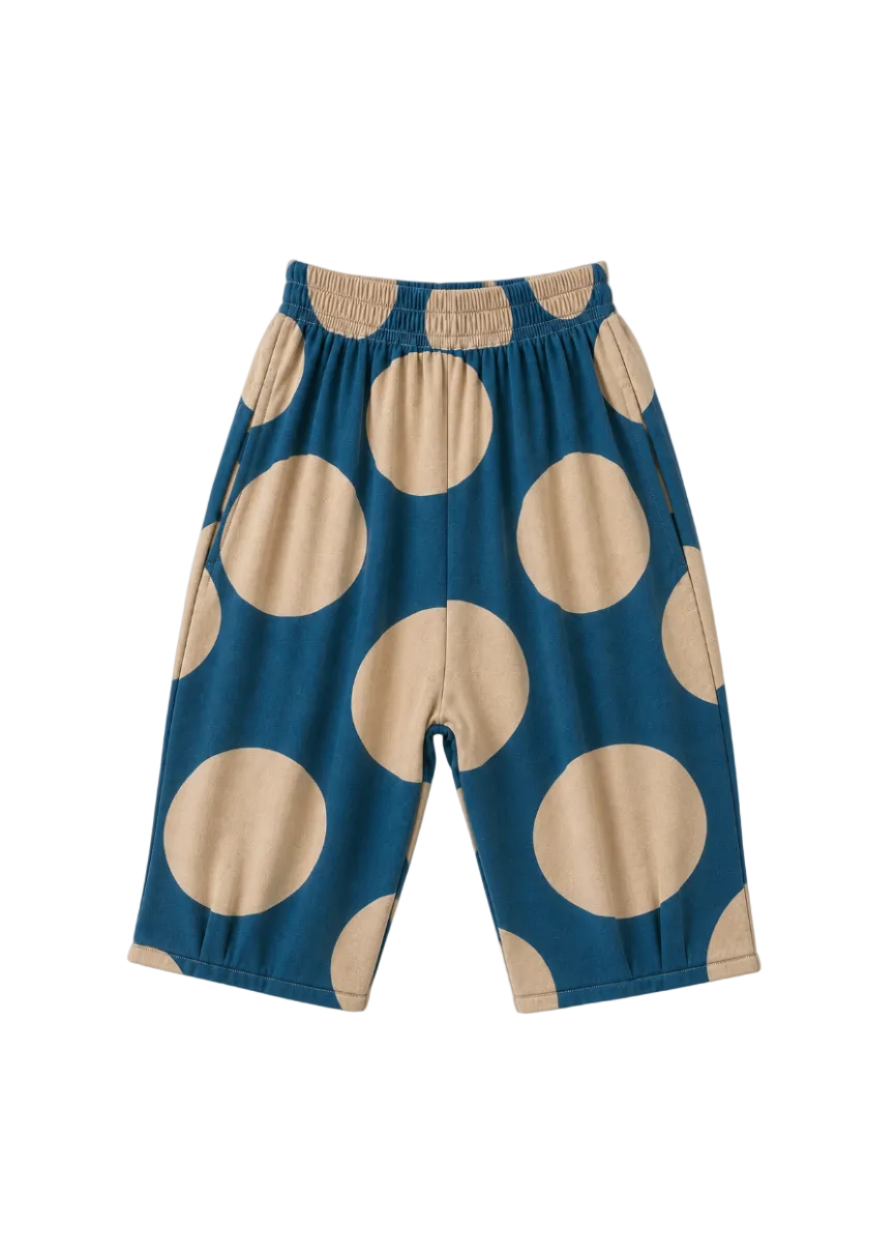 A pair of toddler shorts with a large beige polka dot pattern on a teal blue background, featuring an elastic waistband, shown flat on a light off-white background.