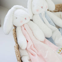 Plush bunny toy with a blanket in a woven basket on a light background