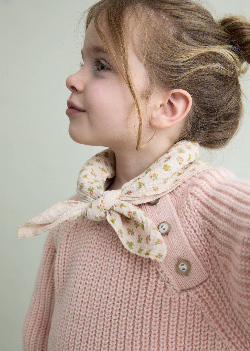 Young girl wearing a pink knitted sweater with a floral bow collar against a light background