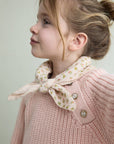 Young girl wearing a pink knitted sweater with a floral bow collar against a light background
