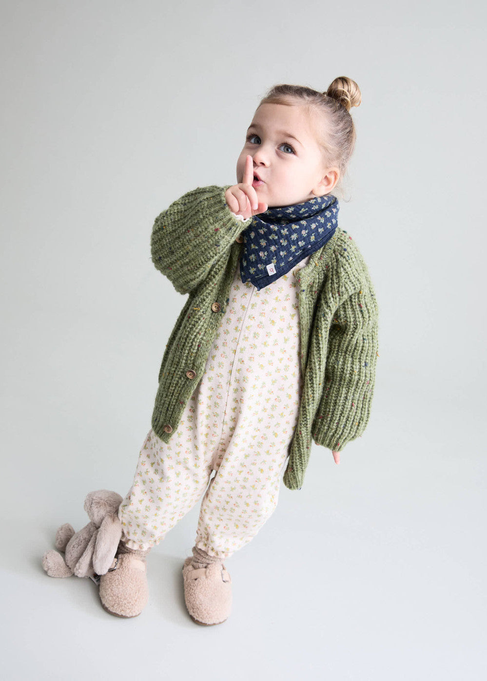Child wearing a green knitted sweater and patterned scarf on a plain background