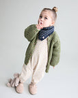 Child wearing a green knitted sweater and patterned scarf on a plain background