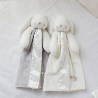 Two plush rabbit toys with scarves, one gray and one white, on a light background.