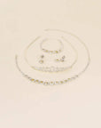 A coordinated jewelry set on a warm cream background, including a silver-tone tiara necklace, matching bracelet, earrings, and a curved collar-style necklace with clear rhinestones.