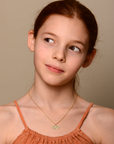Young girl wearing an orange top and gold necklace against a beige background