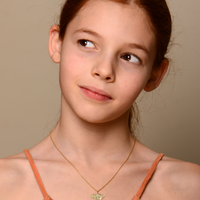 Young girl wearing an orange top and gold necklace against a beige background