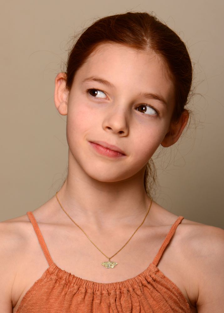 Young girl wearing an orange top and gold necklace against a beige background