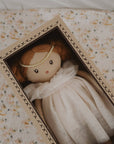 Small doll with a white dress and red hair in a decorative box with floral patterns.