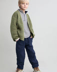 Child wearing a green cardigan, striped shirt, and blue pants on a plain background