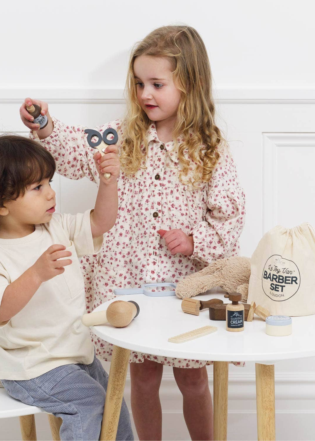 Two children playing with a toy barber set on a white table.