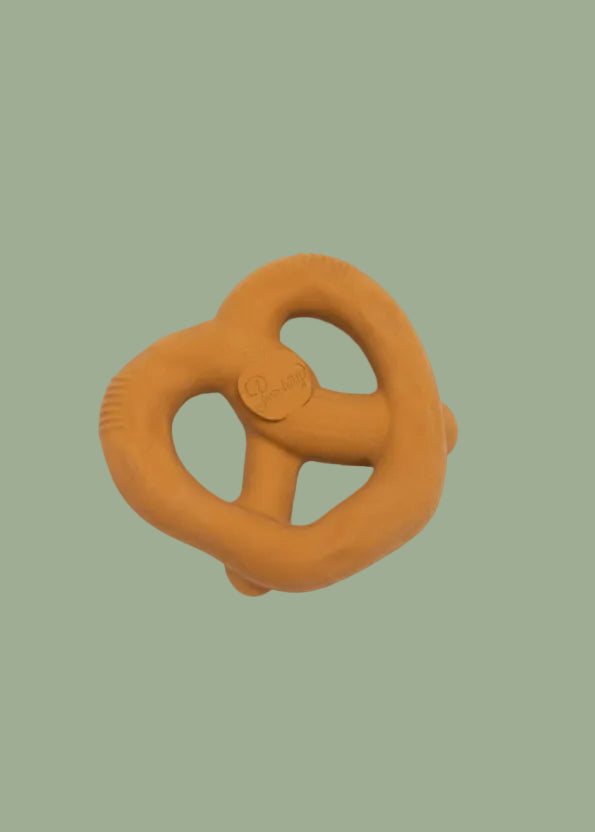 An orange-brown dog chew toy shaped like a pretzel, shown on a solid sage green background. The brand name 'Peanut' is embossed on the center.